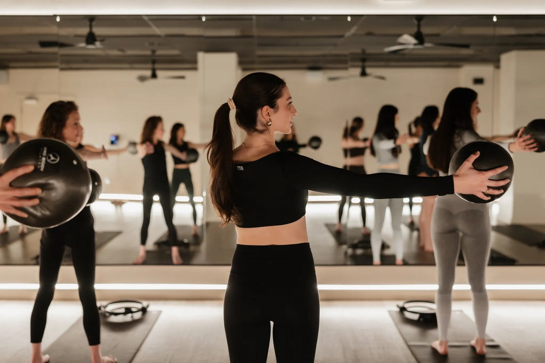 Clients holding Pilates balls with arms extended during a FlowCorps mat class