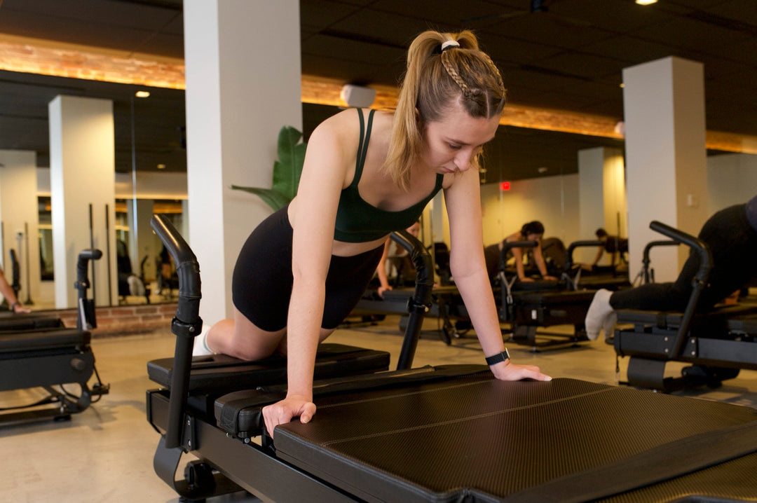 Client kneeling on a Pilates reformer and focusing on core control during a FlowCorps class