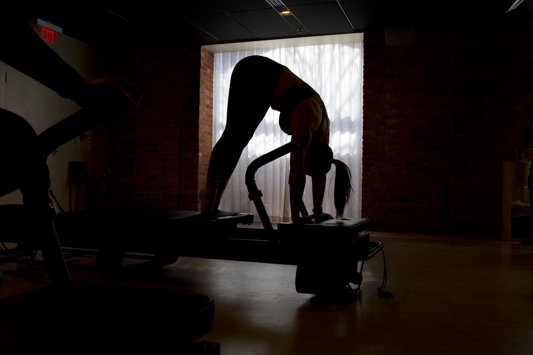FlowCorps Studios client performing a pilates reformer stretch in a dimly lit studio.