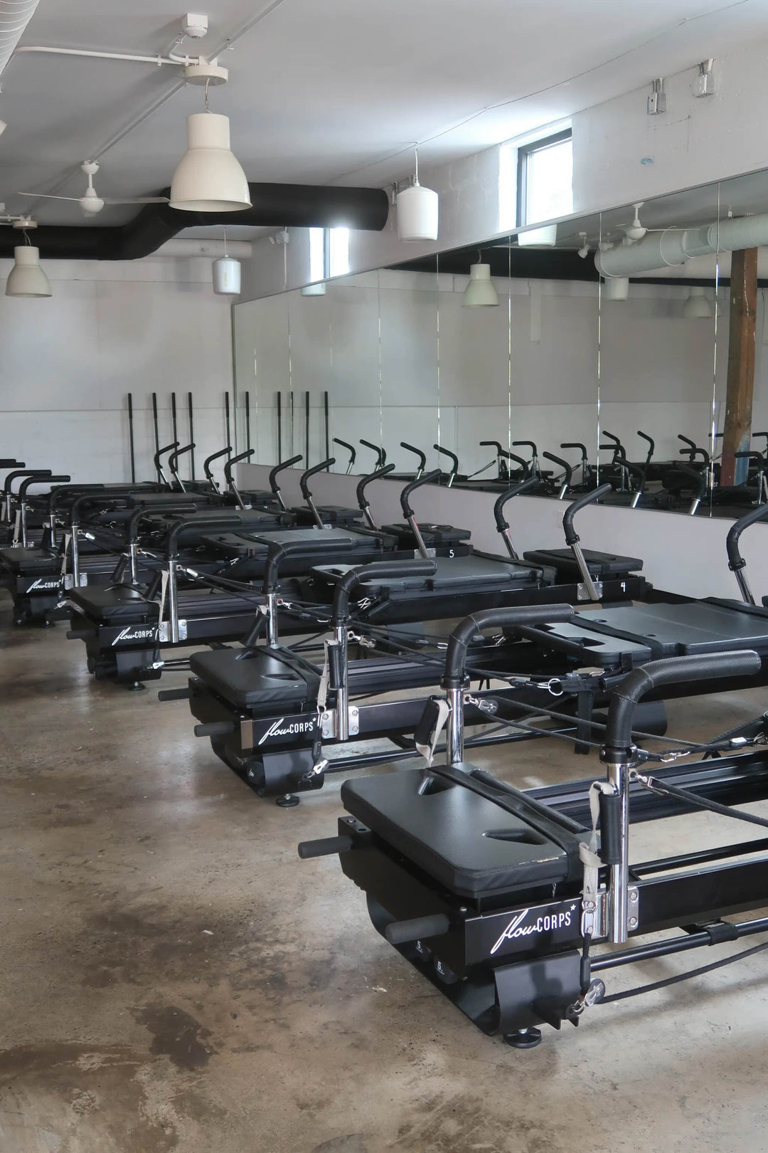 Pilates reformers lined up in a room with mirrors in a FlowCorps studio in Raleigh, NC