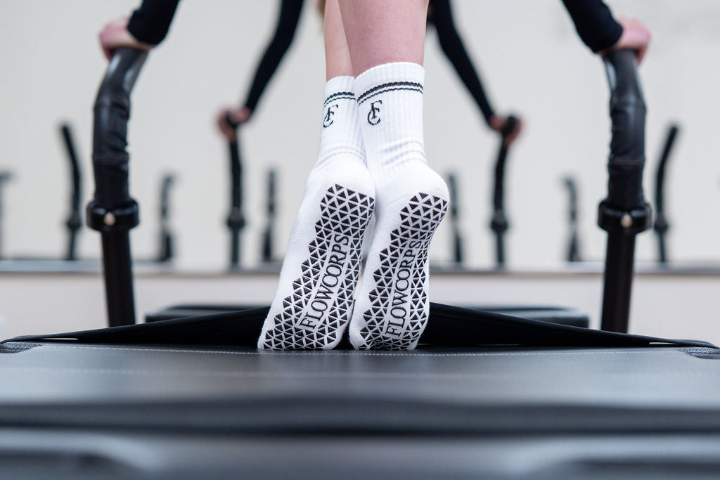 Client in FlowCorps grip socks balancing on tiptoe on a Pilates reformer