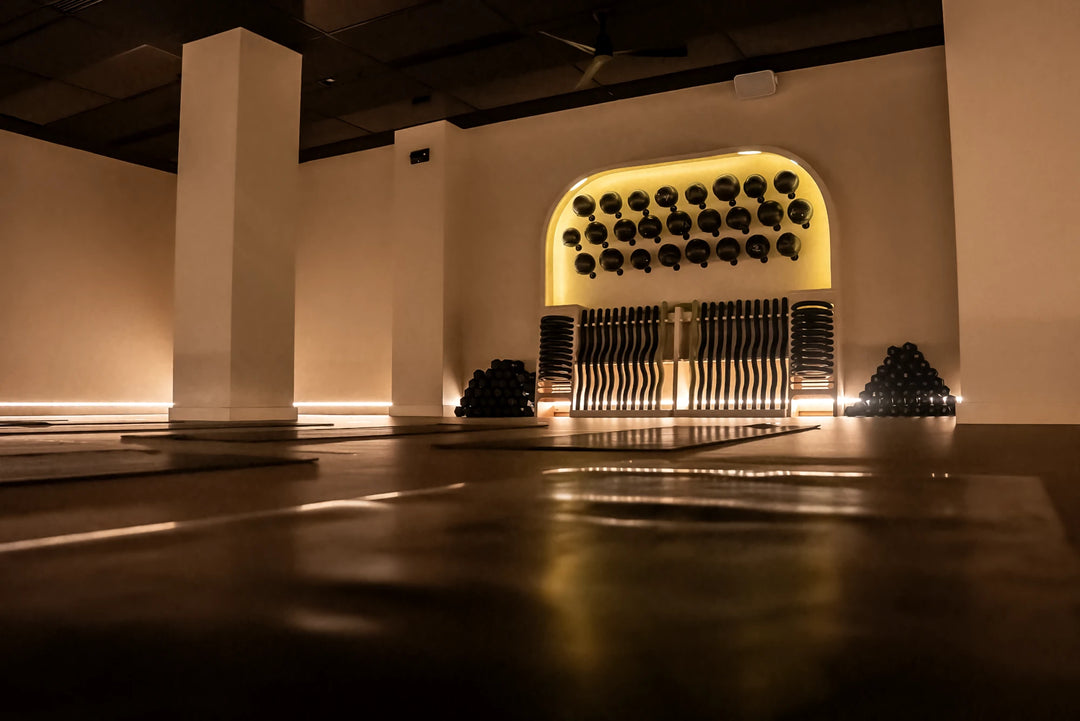 Warmly lit FlowCorps Pilates studio interior with weights and equipment displayed in an arched wall niche